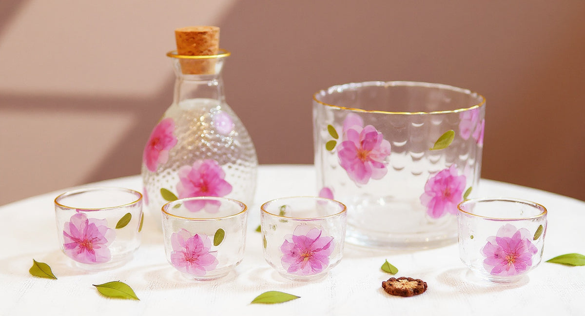Handcrafted sake set with real peach blossoms and gold rim glass on linen table runner.