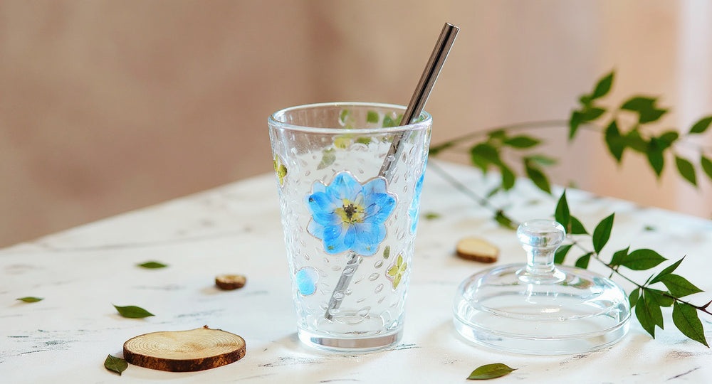 Handmade Floral Glass Cup Real Pressed Flowers with saucer, lid, and glass straw on white marble.
