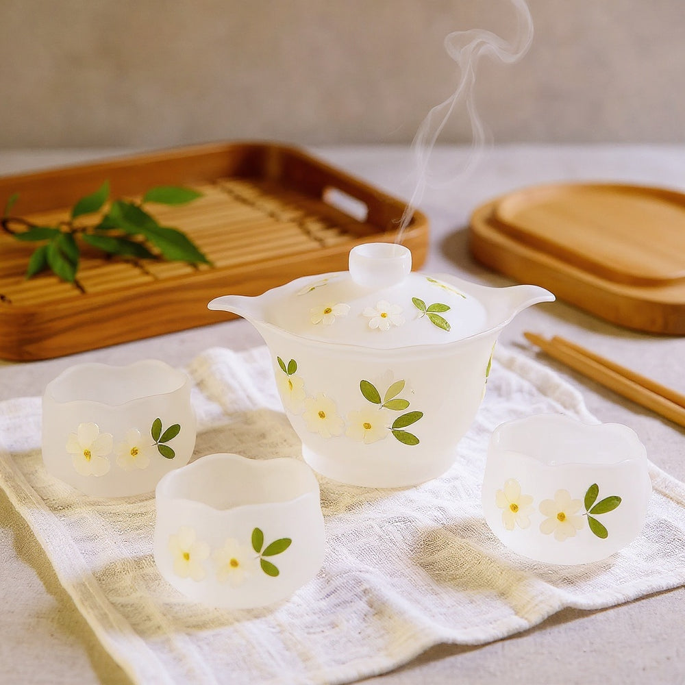 Frosted glass teapot with lotus silhouette and cherry blossom petals, steam rising, on linen with natural wood accents.
