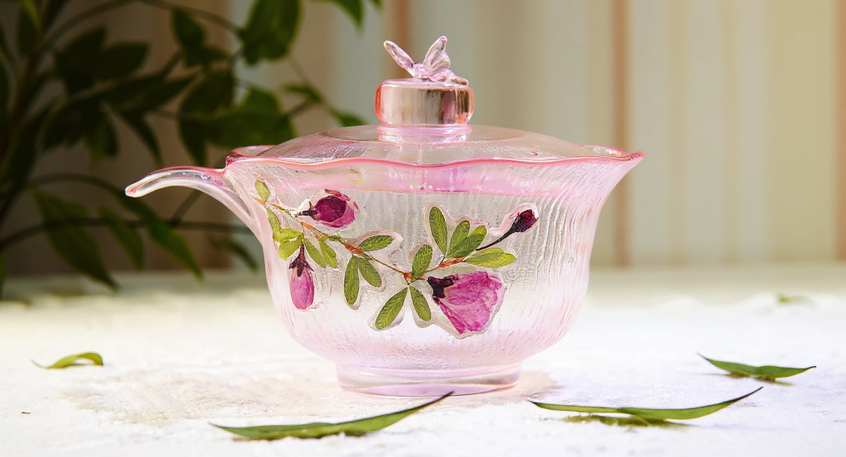 Macro detail of handmade gradient pink butterfly glass cup with raised preserved petals and green leaves