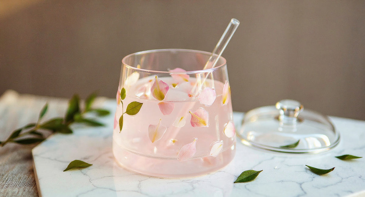 Handcrafted stemless glass with real pink flowers, lid, and straw on marble surface