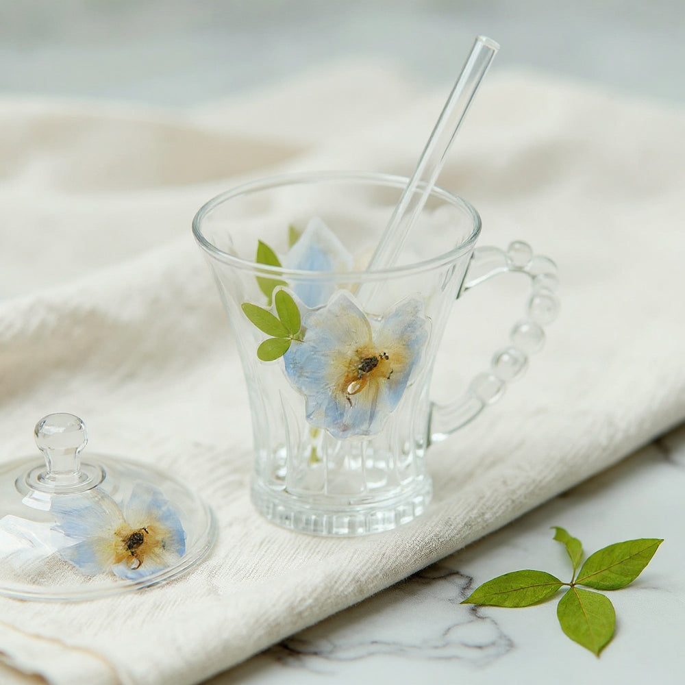 Heat resistant flower glass cup with beaded handle on marble surface with dried flowers
