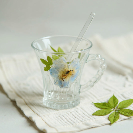 Clear glass cup with dried flowers and beaded handle on linen cloth with loose dried flowers.