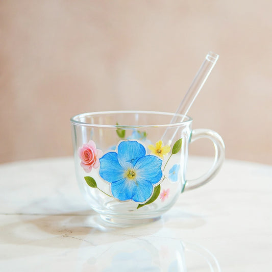 Clear glass cup with preserved floral relief, dust-proof lid, and straw on white marble.