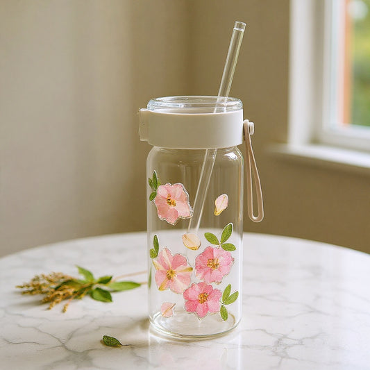 Clear glass tumbler with raised dried flower relief design on marble with loose botanicals, soft natural light.