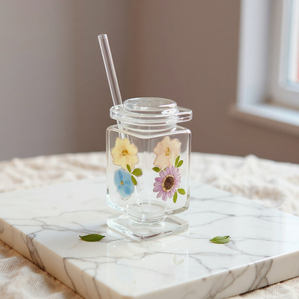 Hero image of a preserved flower embedded drinking glass with soft pastel blooms on a neutral surface