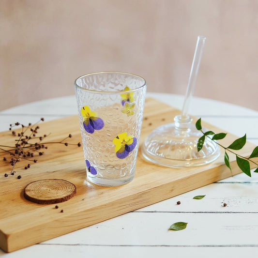 Clear glass cup with preserved flowers and straw on wooden table