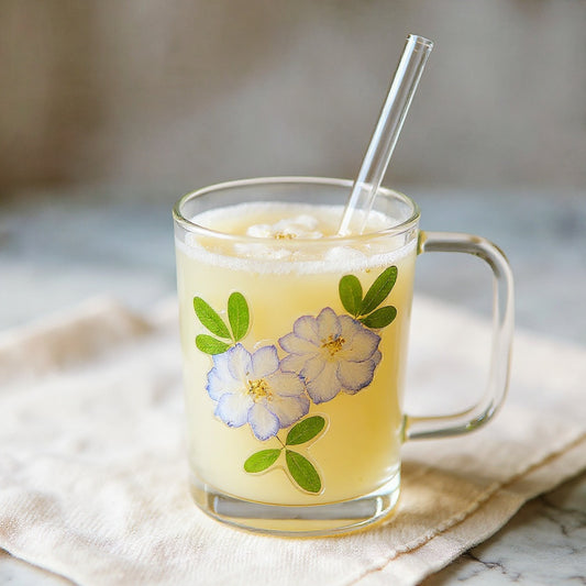 Botanical glass straw cup with embedded flower petals on marble surface