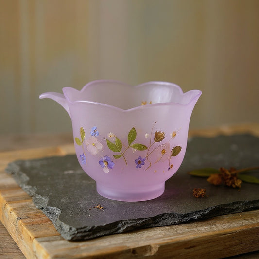 Frosted translucent purple glass lotus cup with embedded botanicals on a rustic wood surface with dried flowers, soft natural light, meditative mood.