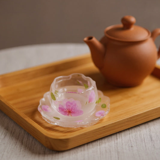 Hero image of an eco-friendly resin drinkware gift: a handmade peach blossom tea cup with embedded flowers on a wooden tray, softly lit in natural light.