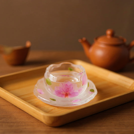 A delicate glass cup with embedded peach blossoms on a wooden tea tray, soft natural light.