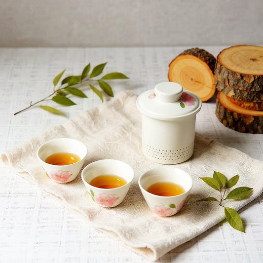 Frosted porcelain gaiwan and teacups with embedded dried flowers on a minimalist natural table setting.