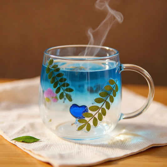 A clear glass mug with raised pressed dried flowers on its exterior, filled with a warm beverage, steam rising, set on a linen surface in soft natural light.
