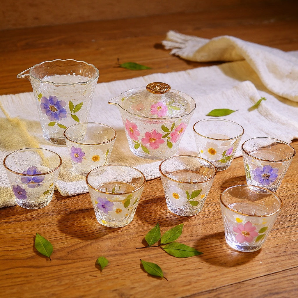 Artisan hammered glass tea set with preserved flowers on a natural wood surface
