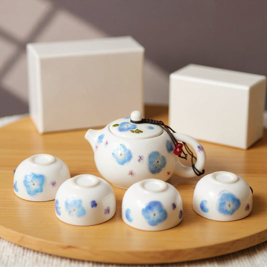 Luminous white porcelain teapot and cups with real pressed blue hydrangea petals on a natural surface