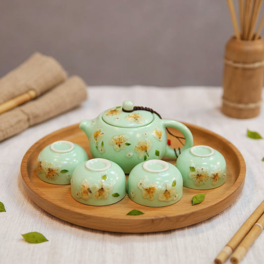 A jade-green celadon porcelain tea set with embedded winter jasmine petals, on a wood tray, styled with natural materials in soft light.