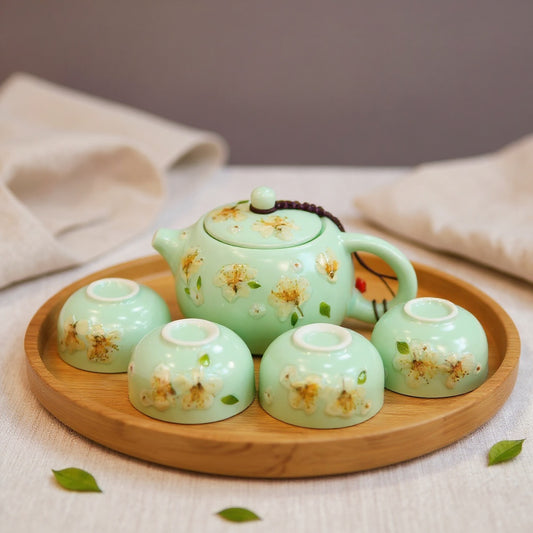 Jade-green celadon teapot and four cups with embedded yellow winter jasmine petals on a wood tray, minimalist Zen arrangement with soft natural light and natural props.