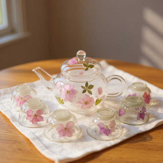 Glass teapot and cups with real dried flowers on linen, soft natural lighting.