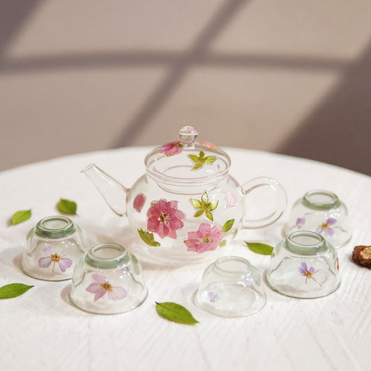 A heat-resistant glass tea set with embedded pressed flowers on a linen background, hero image with soft lighting.