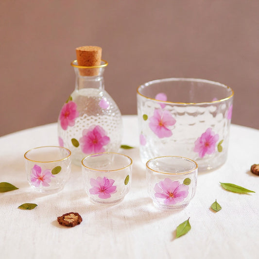 Photorealistic editorial image of a handcrafted sake set with real peach blossoms on a neutral linen surface.