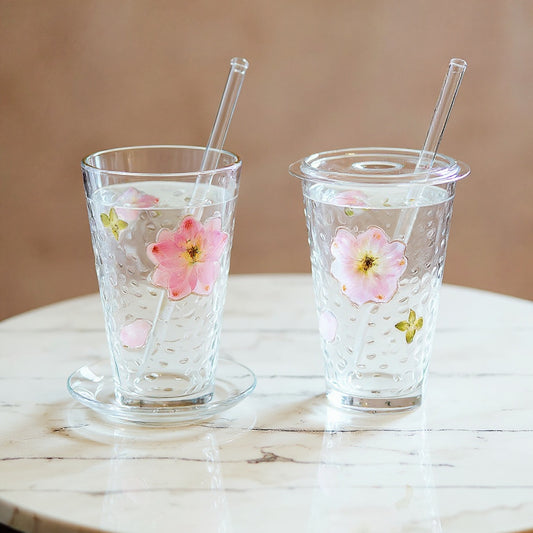 Handmade floral glass cup with matching saucer, lid, and straw on marble surface in natural light