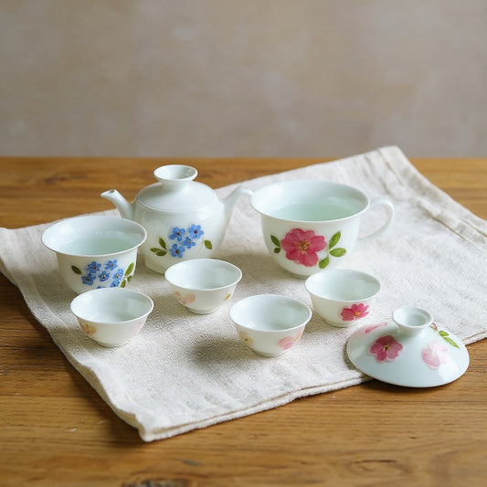 A delicate warm-white porcelain gaiwan and matching teacups with raised flower petal relief on a linen cloth, softly lit.
