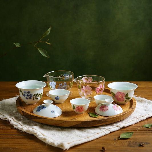 Semi-translucent porcelain tea set with preserved flower petals on linen, with eucalyptus, against bold sage background, dramatic lighting.
