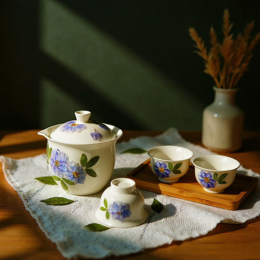 Aesthetic botanical porcelain tea set displayed on a wooden tray with pampas grass and scattered petals against a bold sage green background.