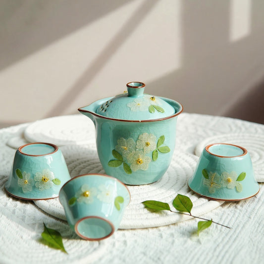 Handmade ruyao celadon teapot and cups with real flower inclusions on linen