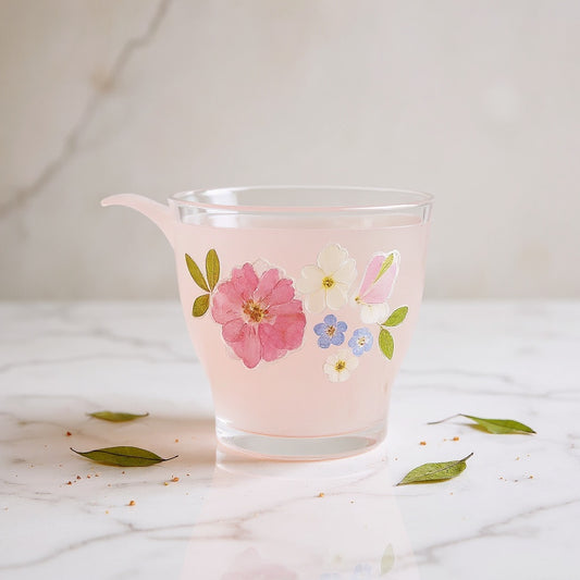 Delicate clear glass cup with pink gradient and preserved flowers on marble with dried botanicals