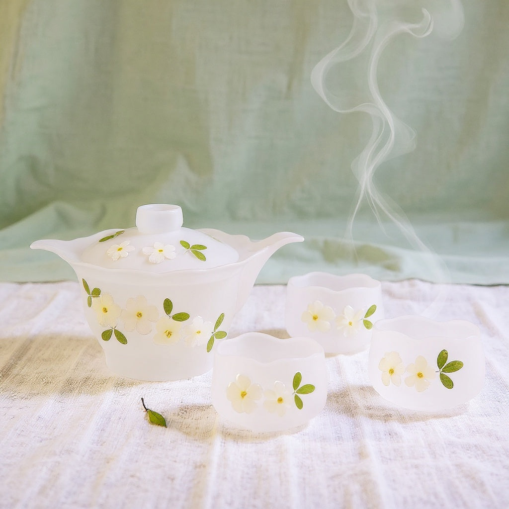 Handmade glass teapot set with real cherry blossom petals on linen background