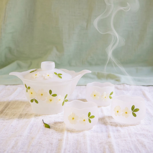 Handmade glass teapot set with real cherry blossom petals on linen background