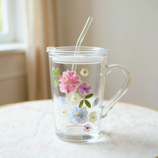 Clear glass tumbler with real pressed flowers and dust-proof lid, on marble surface with soft window light.