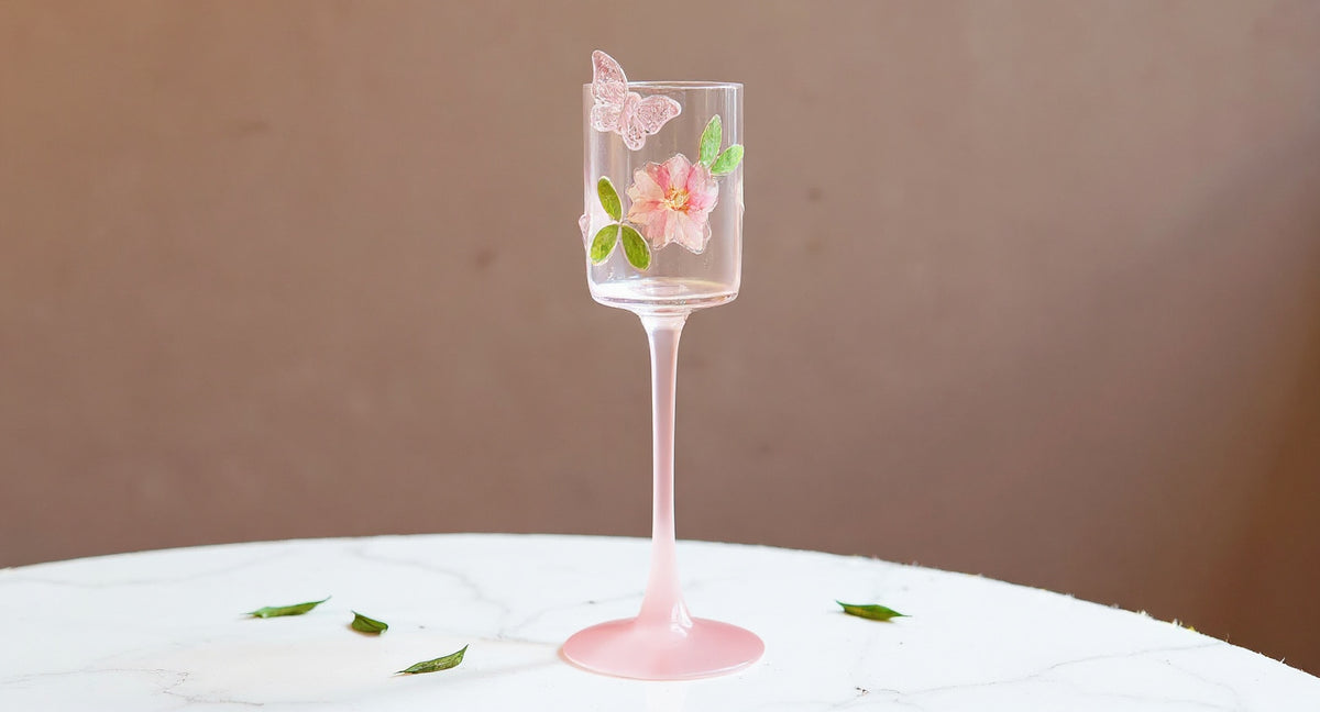 Handmade Floral Champagne Flute with preserved pink petals and green leaves on white marble.
