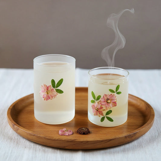 Frosted glass gaiwan and fair cup with embedded dried botanicals, steam rising, on linen with wooden tray, warm natural light.