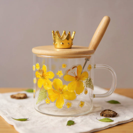 Clear glass mug with embedded real dried flowers, bamboo lid, and wooden spoon on a linen background with soft natural light.