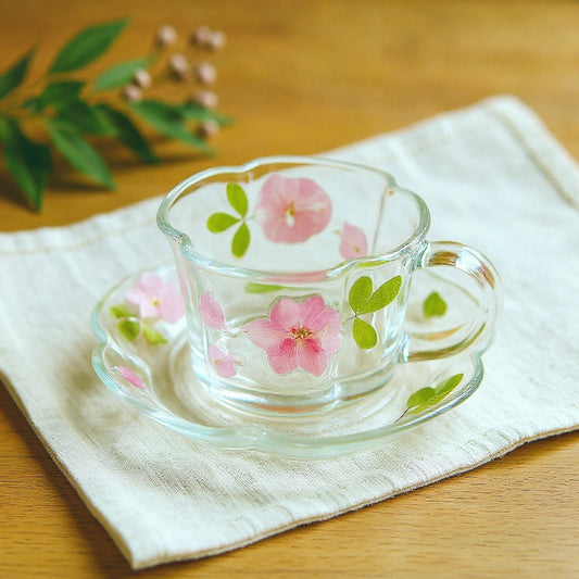 Handmade glass cup and saucer with floral relief on linen cloth with dried flowers, wide shot.