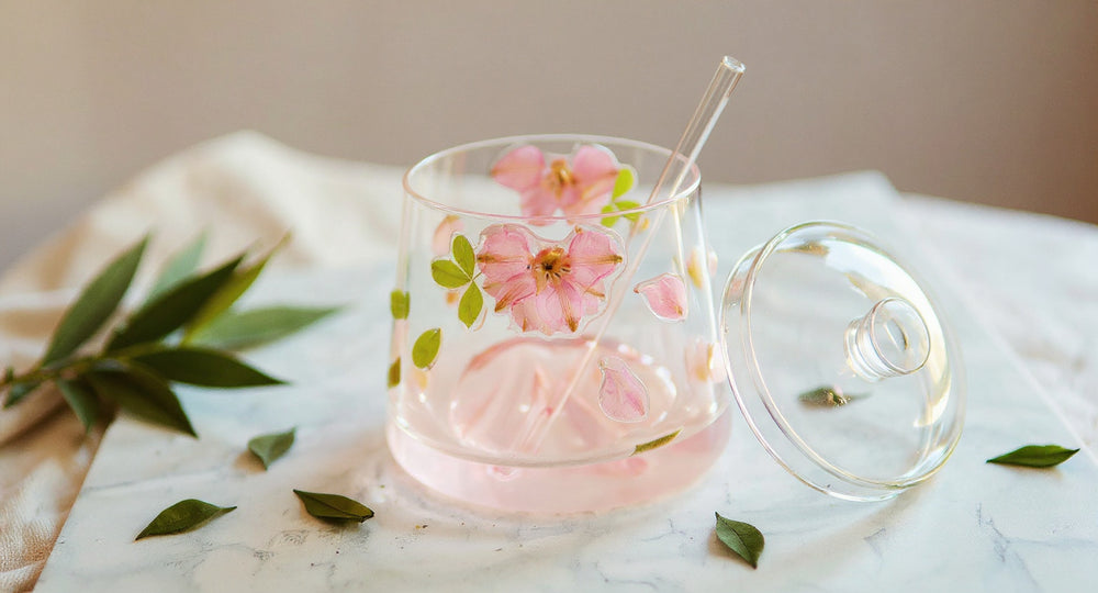 Stemless wine glass with real pink flowers inside on white marble with peonies and straw.