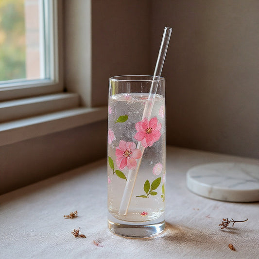 Transparent glass tumbler with pressed flower relief and clear straw on linen surface with soft window light and botanical accents.