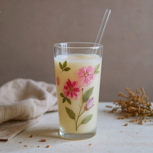 Transparent borosilicate glass tumbler with raised floral relief and glass straw, styled on a linen surface with soft natural light.